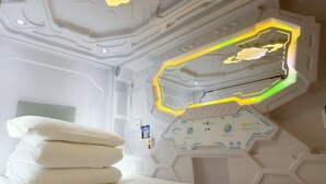 Une chambre moderne avec un plafond au design géométrique, un panneau de contrôle doté de divers réglages et des coussins soigneusement disposés sur le lit.