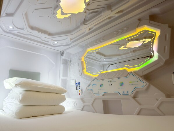 Une chambre moderne avec un plafond au design géométrique, un panneau de contrôle doté de divers réglages et des coussins soigneusement disposés sur le lit.