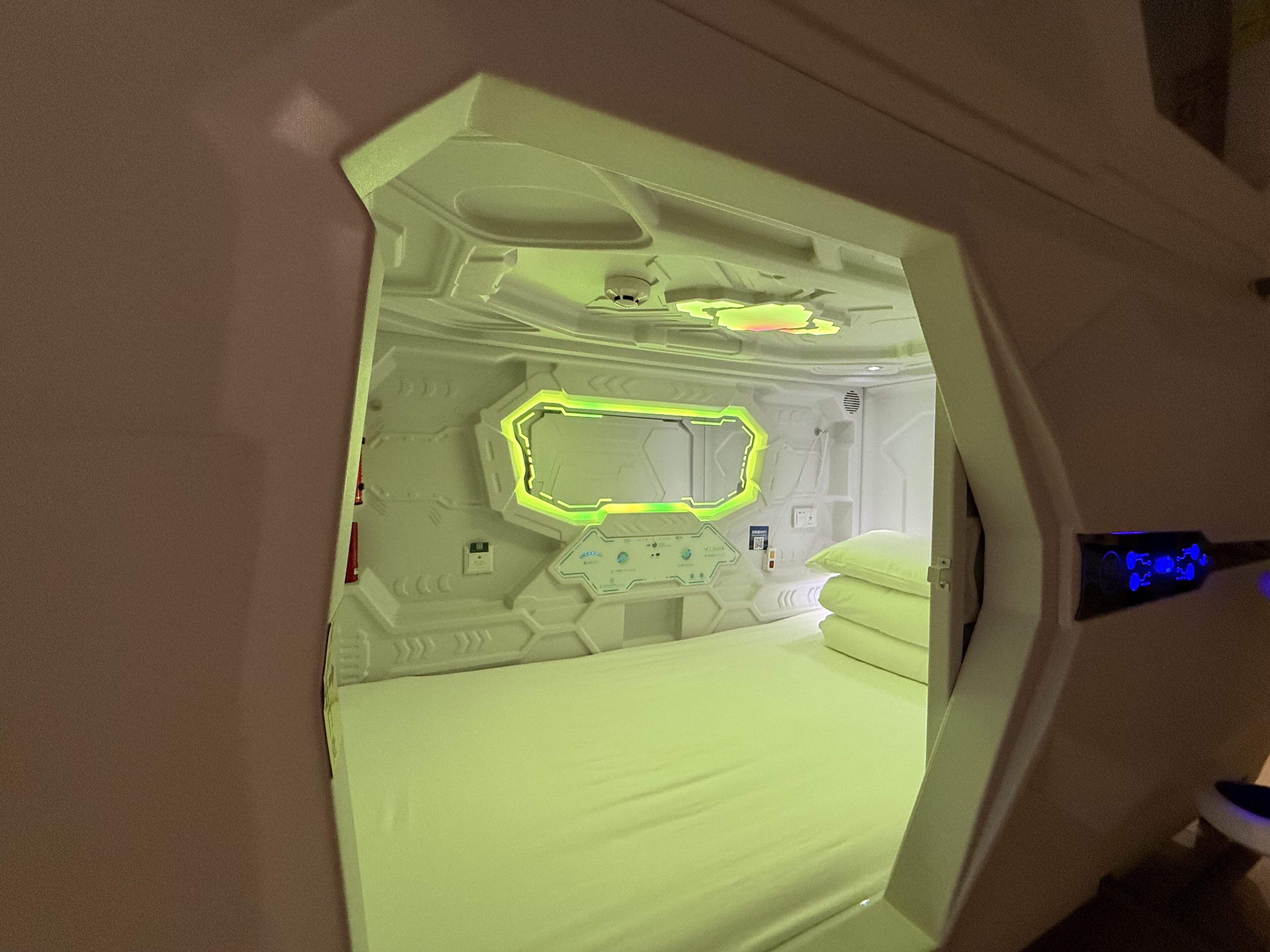 Ein Zimmer mit einem Bett, einer Bedienkonsole und einer neonbeleuchteten geometrischen Wandgestaltung.