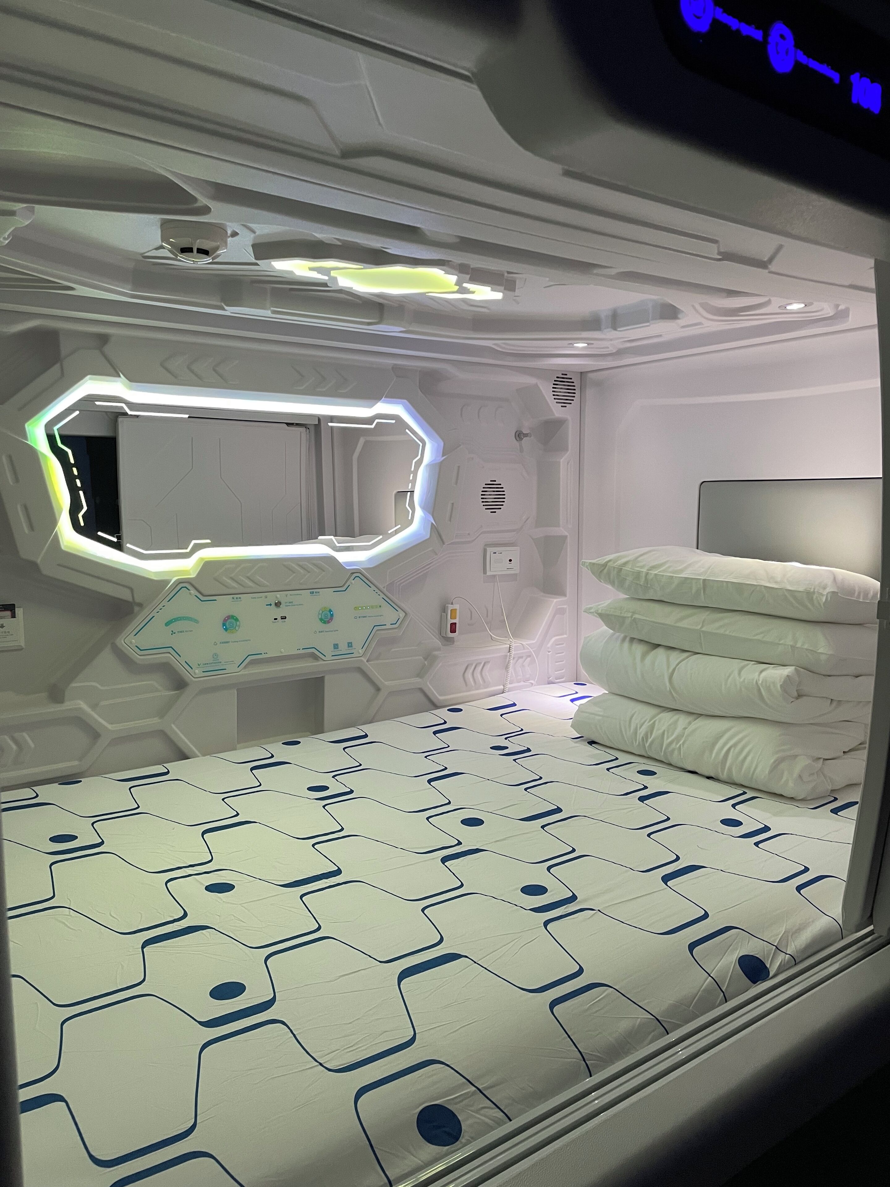 Une pièce futuriste avec un lit aux motifs géométriques, un panneau de contrôle et une fenêtre à cadre hexagonal.