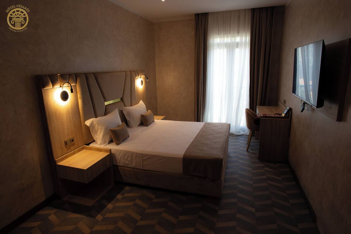 A modern hotel room with a large bed, bedside tables, a desk, and a flat-screen TV.