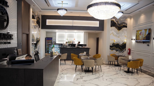 Un vestíbulo de hotel moderno con suelo de mármol, un mostrador de recepción, sillas amarillas y una zona de bar.