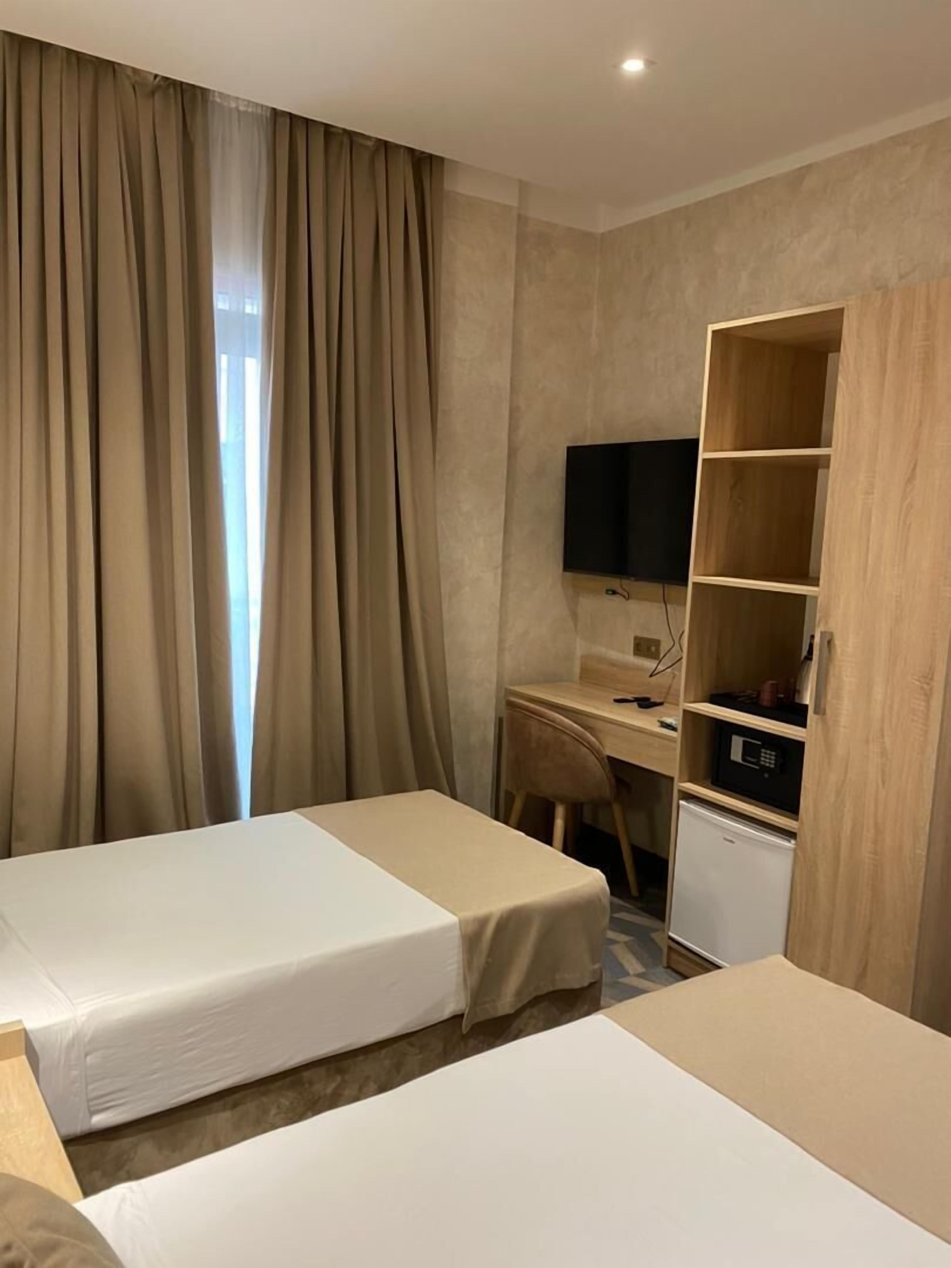 A hotel room with two beds, a desk with a computer, a TV, and a minibar.