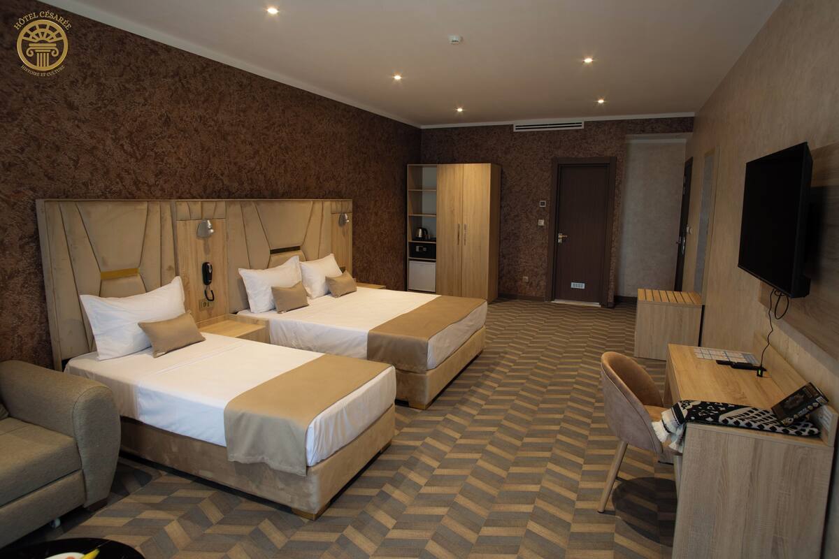 A hotel room with two beds, a desk, a chair, a TV, and a wardrobe.
