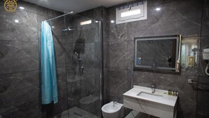 Un baño moderno con ducha de vidrio, lavamanos blanco y un bidé.