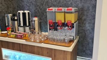 A beverage station with multiple drink dispensers, cups, and a refrigerator.