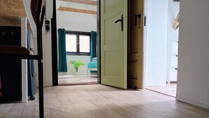 A hallway with wooden flooring leading to a room with a bed, a window with curtains, and a door. - Ferienhaus Meurastein (Meura)