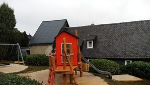 A playground with a red playhouse, a slide, and a swing set. - Ferienhaus Meurastein (Meura)