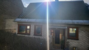 A house with a sloped roof, a brick wall, and a wooden door. - Ferienhaus Meurastein (Meura)