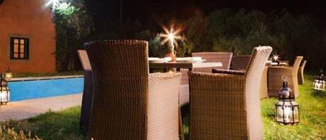 An outdoor dining area with wicker furniture and a pool in the background.