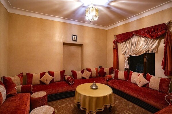 A room with a red sofa set, a round table, and a chandelier. - Riad Harouak (Souihla)