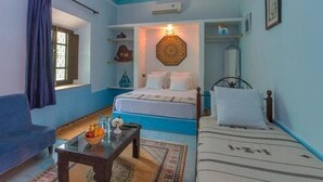 Une pièce comprenant un lit, un canapé, une petite table avec un panier de fruits, un tapis à motifs et une décoration murale.