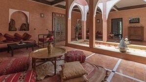 Un intérieur spacieux avec un plafond haut, des alcôves en arc de cercle, un espace salon central avec une table ronde et une fontaine décorative.
