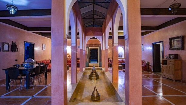 Un hall d’entrée spacieux agrémenté d’une fontaine centrale, de colonnes en arc de cercle et d’un espace repas avec une table et des chaises.