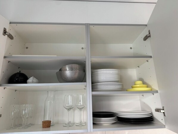 Ein Küchenschrank mit Regalen, gefüllt mit verschiedenen Küchenutensilien, darunter Schüsseln, Tellern und Gläsern.