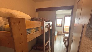 A narrow hallway with bunk beds on one side and a door leading to a room with a table and chairs. - Ski studio at the foot of the slopes Valfréjus ski resort (Valfréjus)