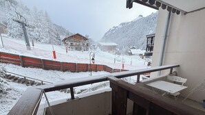 A snow-covered balcony with a view of a ski slope, a wooden building, and a chairlift. - Ski studio at the foot of the slopes Valfréjus ski resort (Valfréjus)