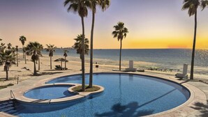 Ein Pool mit gewölbter Kante, umgeben von Palmen und einem Strand im Hintergrund.