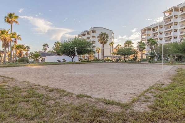 A sandy volleyball court surrounded by palm trees and buildings.