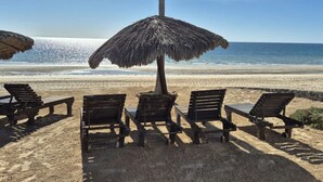 Ein Strand mit Holzliegen und einem Reetdachschirm, mit Blick auf den Ozean.