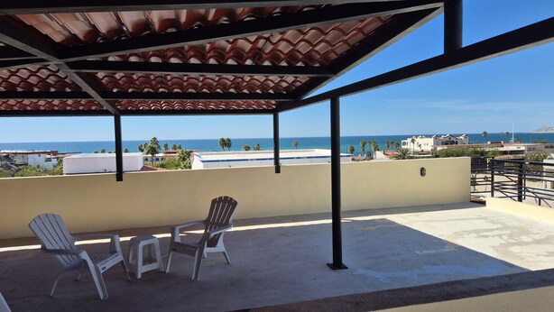 Uma área de estar coberta ao ar livre, com duas cadeiras e uma mesa, com vista para a costa.