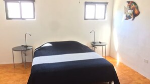 Quarto com cama, duas mesinhas de cabeceira, uma janela e um enfeite de peixe na parede.