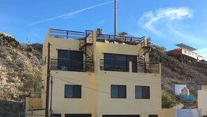 Um edifício de vários andares com telhado plano, uma escadaria no segundo andar e uma antena grande no topo.