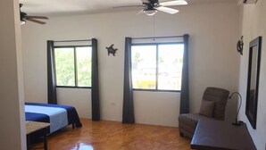 Une chambre avec deux lits, un bureau, une chaise et un ventilateur de plafond.
