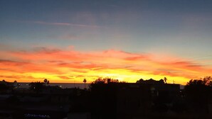 Un coucher de soleil avec un croissant de lune, un ciel dégagé et les silhouettes de bâtiments et d’arbres.