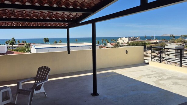 Un balcon avec vue sur la mer, une chaise et un toit recouvert de tuiles.