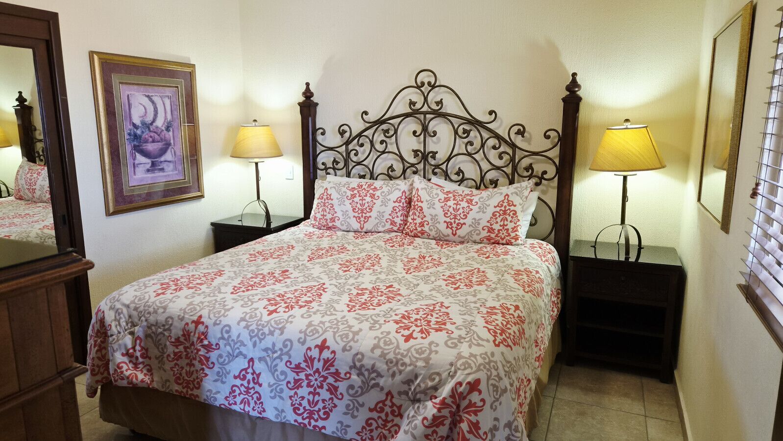 A bedroom with a bed, two bedside tables, two lamps, a dresser, and a framed picture on the wall.