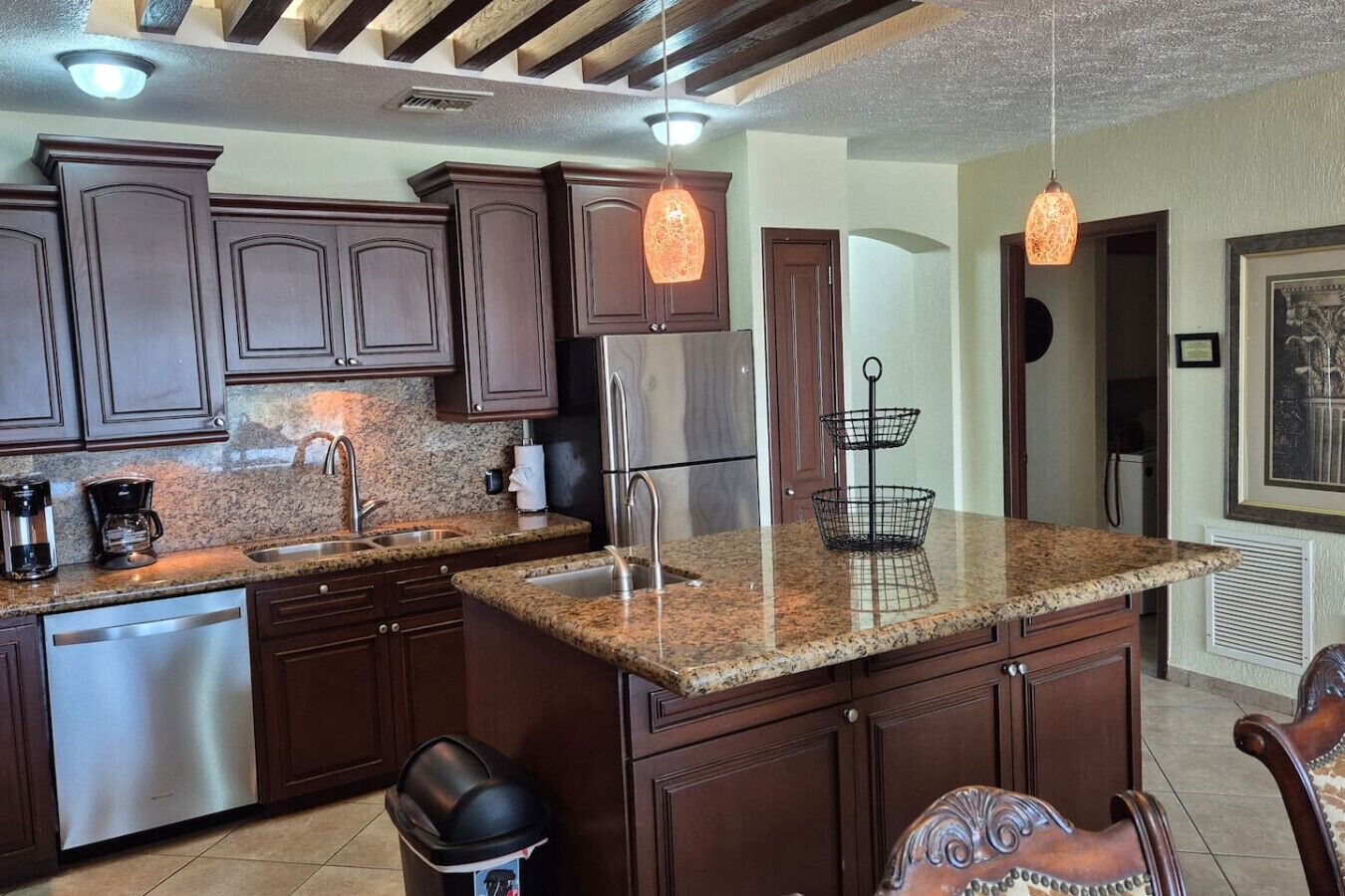 A kitchen with dark wood cabinets, granite countertops, stainless steel appliances, and pendant lighting.