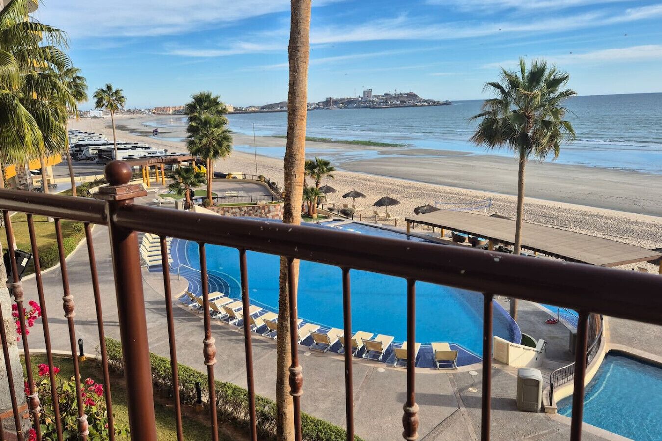 Zona de piscina con sillones de descanso, palmeras y vistas a la playa y al océano.