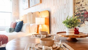 A dining area with a round table set for two, a sofa with cushions, a lamp, and a wall with a geometric pattern. - Hotel California - KING BED LOFT (Ypsilanti)
