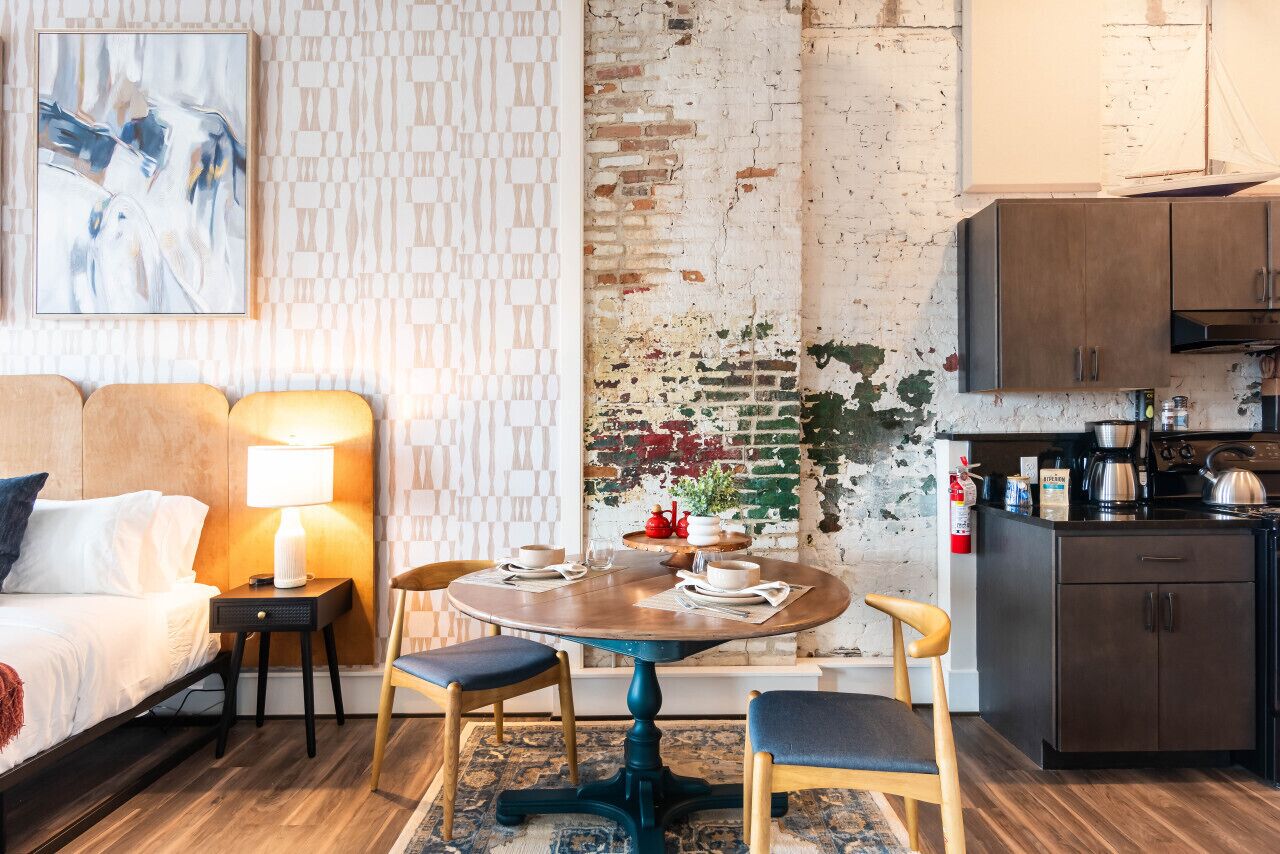 Une chambre d’hôtel confortable, équipée d’un lit, d’une table de chevet, d’une lampe et d’un coin repas avec une table et des chaises.