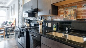 A kitchen with stainless steel appliances, a black countertop, and a brick wall. - Hotel California - KING BED LOFT (Ypsilanti)