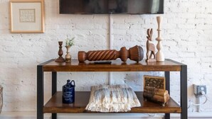 A wooden console table with a flat-screen TV above it, placed against a white brick wall. - Hotel California - KING BED LOFT (Ypsilanti)