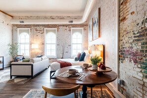Una habitación con cama, sofá, mesa de comedor y sillas, y ventanas amplias.