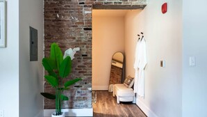 Ein schmaler Flur mit Backsteinwand, einer Topfpflanze, einer weißen Bank und einem Spiegel an der Wand.