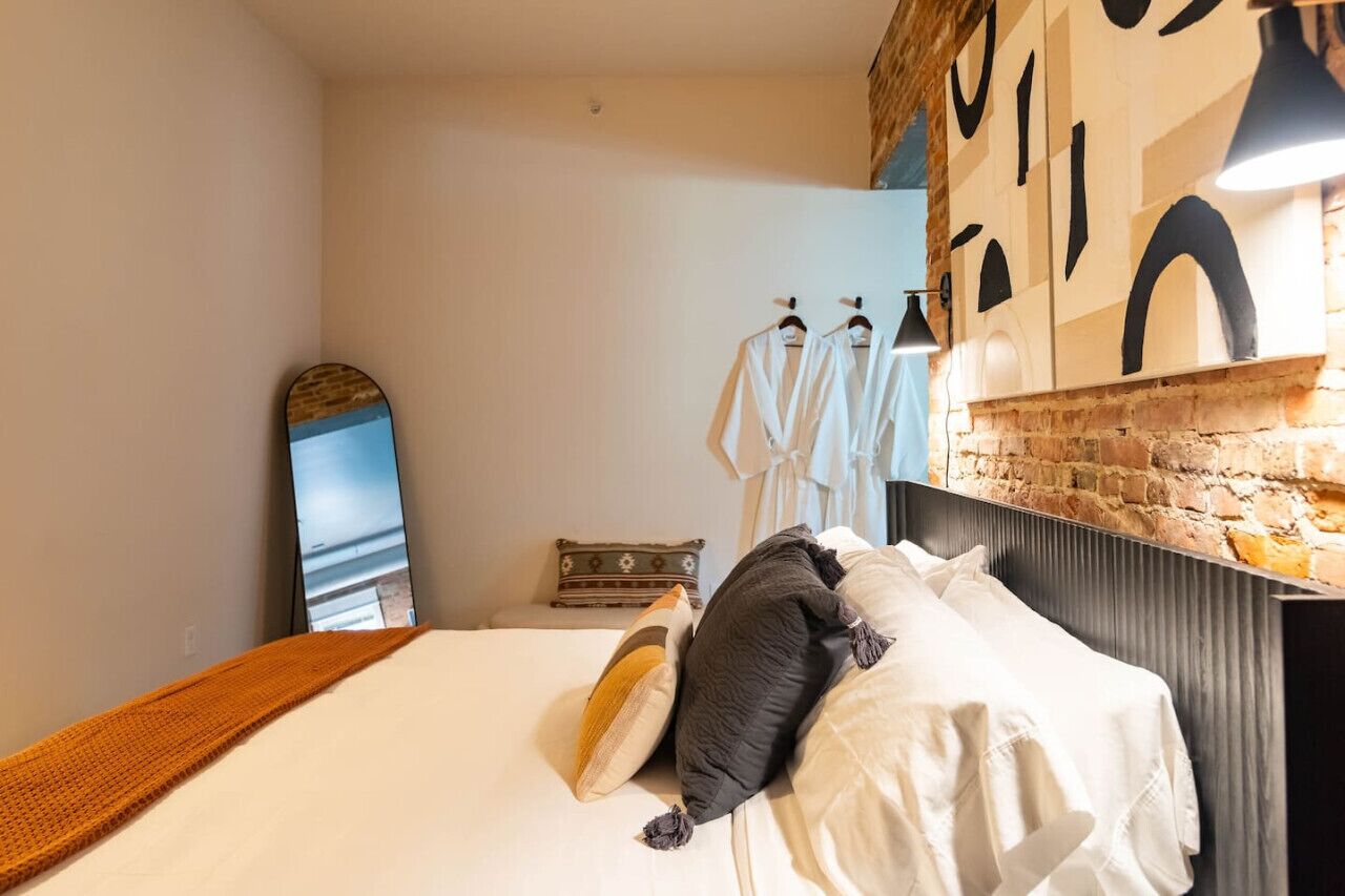 A hotel room with a bed, pillows, a blanket, a mirror, and a wall with a brick pattern.