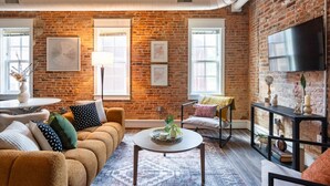 Ein gemütliches Wohnzimmer mit Backsteinwand, einer Couch, einem Couchtisch und einem Fernseher.