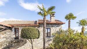 Un edificio in pietra con tetto a tegole, un piccolo balcone e una palma sullo sfondo.