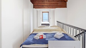 Camera da letto con soffitto in legno, un letto con copriletto blu, cuscini bianchi e una finestra con vista.
