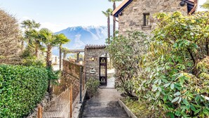 Un edificio in pietra con tetto in tegole, un cancello e un sentiero che vi conduce, immerso nel verde e tra palme.