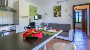 A modern kitchen with a gas stove, oven, and a dining area with a sofa and a table set for two. - Le Farsiche by Interhome (Castellina Marittima)