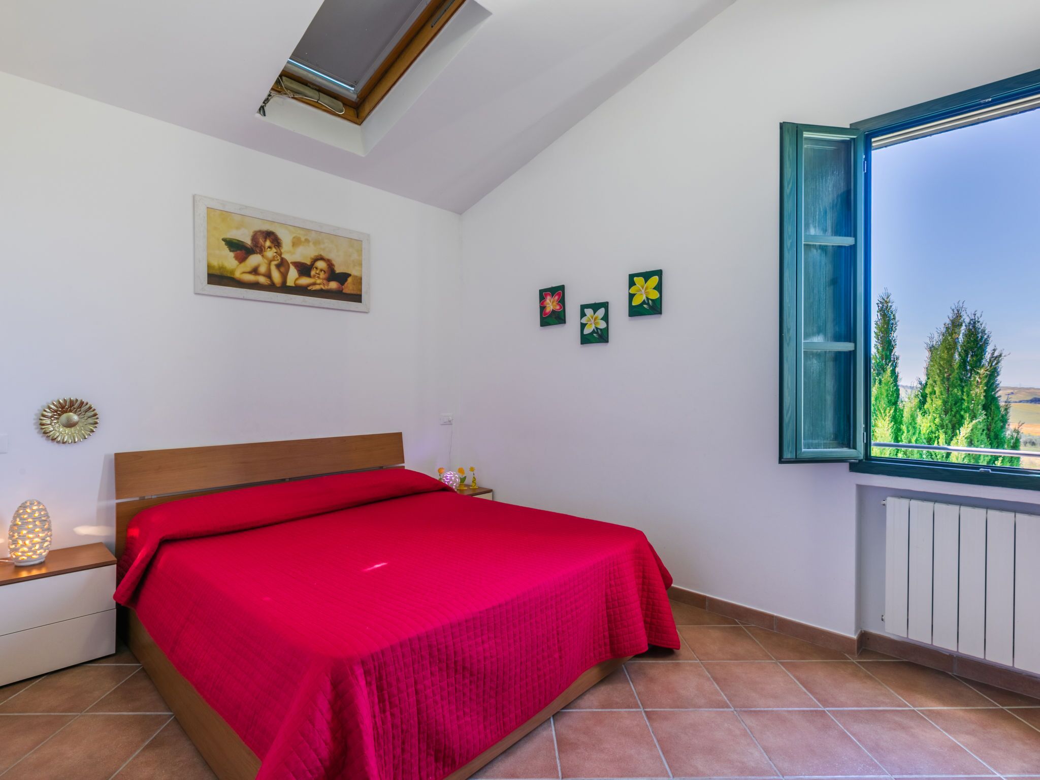 A bedroom with a bed, a painting, and a window with a view of trees.