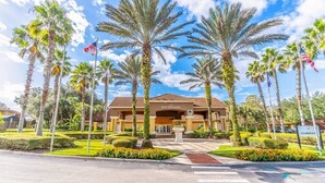 A hotel entrance with palm trees, a clear sky, and an American flag. - Encantada Resort Townhome with Pool Near Disney (Kissimmee)