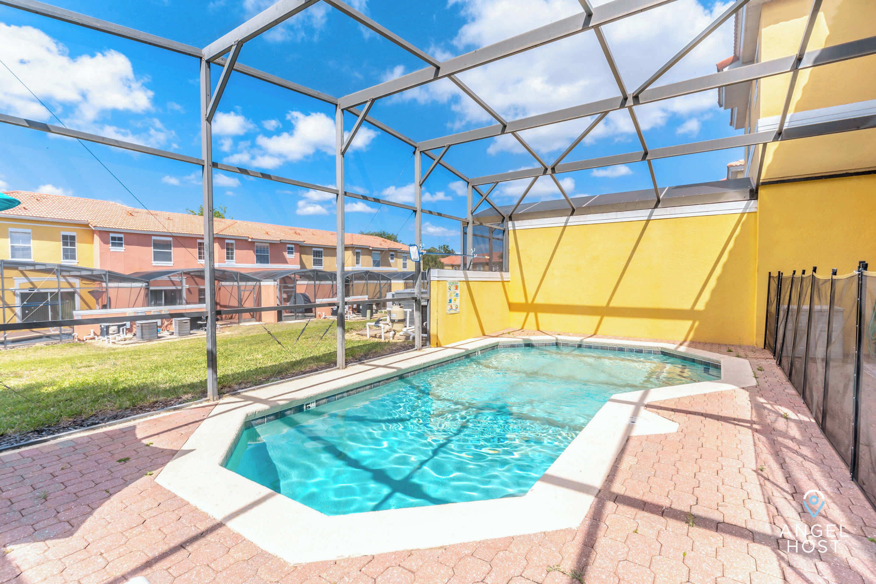 A swimming pool with a clear blue water, surrounded by a brick patio and a glass enclosure.