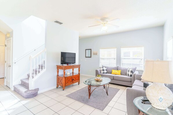 A living room with a staircase, a sofa, a glass coffee table, and a television.