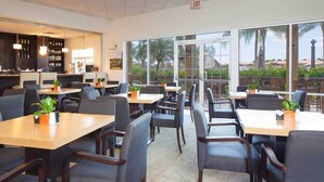 A restaurant with multiple tables and chairs, a bar area with bottles, and large windows offering a view of palm trees and buildings. - Encantada Resort Townhome with Pool Near Disney (Kissimmee)